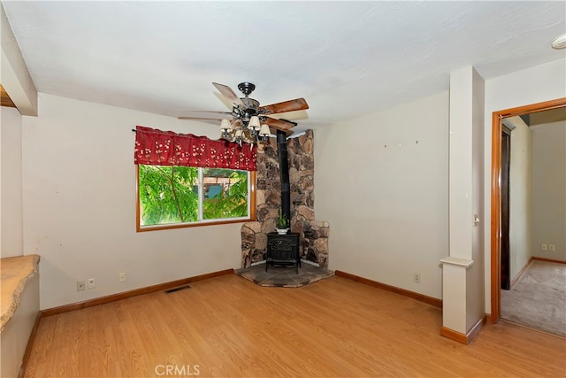 unfurnished living room featuring ceiling fan, light wood-type flooring, and a wood stove