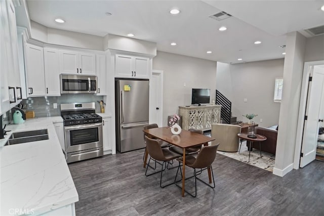 kitchen featuring sink, dark wood-type flooring, white cabinetry, appliances with stainless steel finishes, and light stone countertops