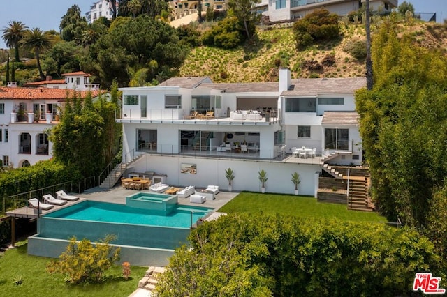 back of house featuring a lawn, a balcony, a patio area, and an in ground hot tub