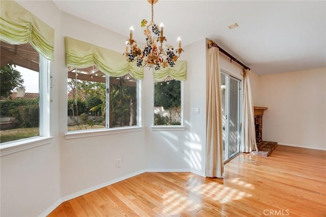 unfurnished dining area with hardwood / wood-style flooring, a fireplace, and an inviting chandelier