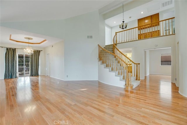 unfurnished living room with high vaulted ceiling, a notable chandelier, light wood-type flooring, and a wealth of natural light