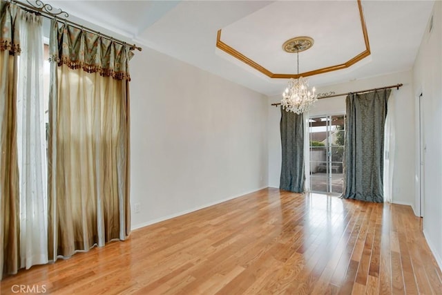 spare room with a tray ceiling, an inviting chandelier, and hardwood / wood-style flooring