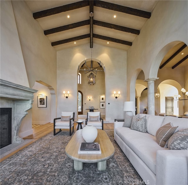 living room featuring a fireplace, high vaulted ceiling, a notable chandelier, beamed ceiling, and hardwood / wood-style floors