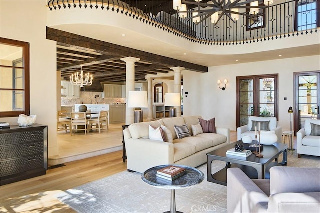 living room featuring beamed ceiling, a towering ceiling, light hardwood / wood-style floors, and ornate columns