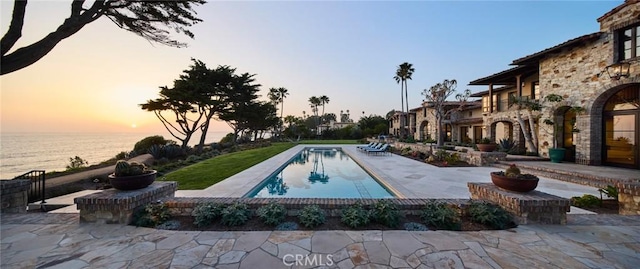 pool at dusk featuring a water view and a patio