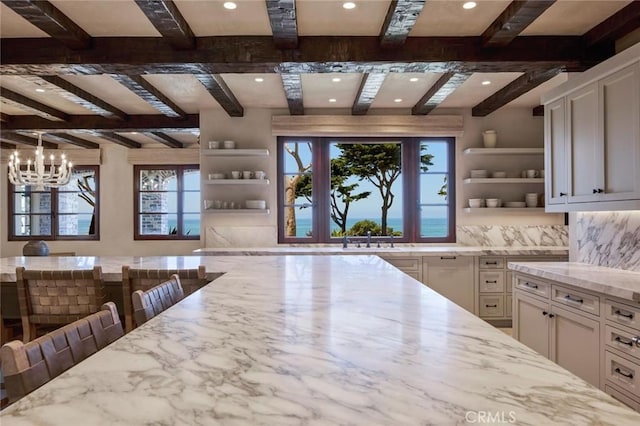 kitchen with decorative backsplash, light stone counters, a breakfast bar, a chandelier, and white cabinetry