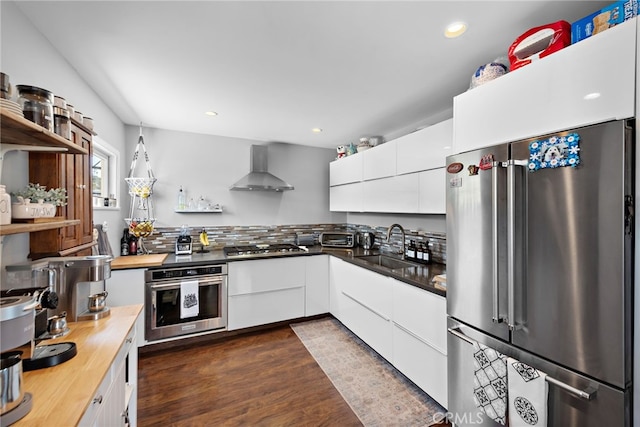 kitchen with white cabinets, wall chimney range hood, sink, appliances with stainless steel finishes, and dark hardwood / wood-style flooring