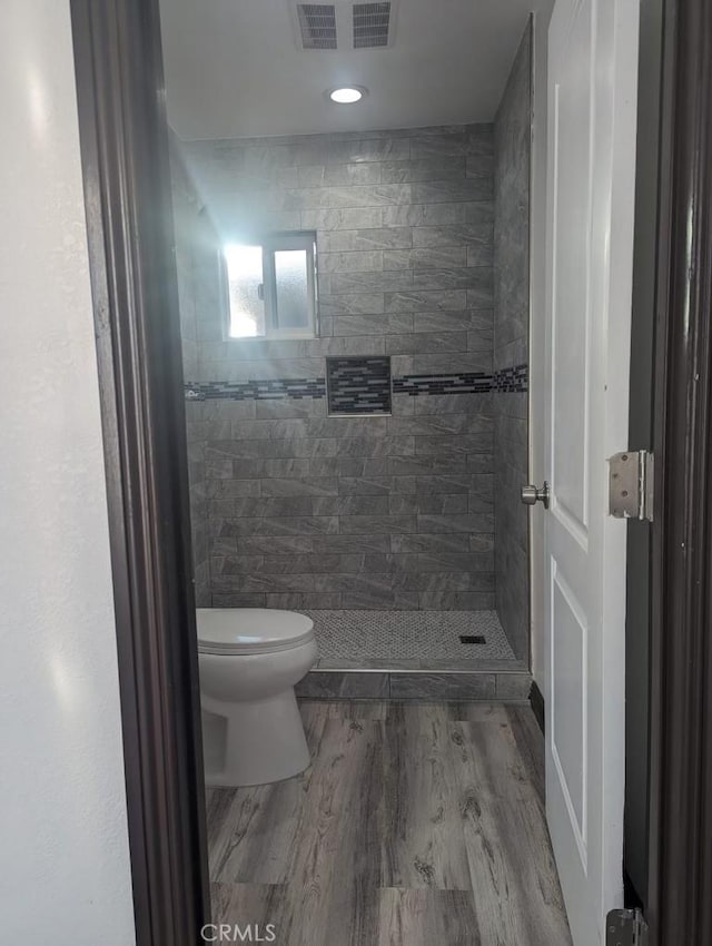 bathroom featuring tiled shower, hardwood / wood-style flooring, and toilet