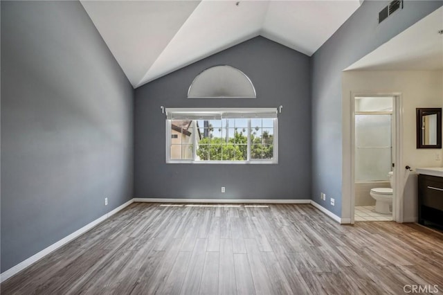 unfurnished bedroom featuring ensuite bath, light hardwood / wood-style floors, and lofted ceiling