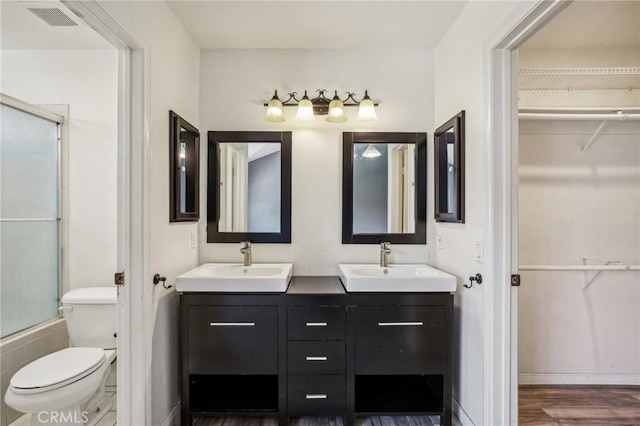 full bathroom featuring hardwood / wood-style floors, vanity, combined bath / shower with glass door, and toilet