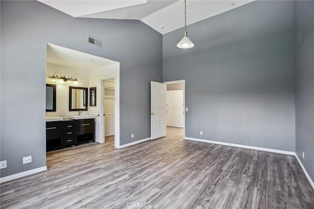 unfurnished bedroom featuring high vaulted ceiling, ensuite bath, light hardwood / wood-style floors, and sink