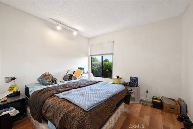 bedroom with rail lighting, wood-type flooring, and a textured ceiling