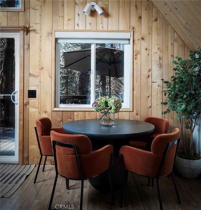 dining room with wood walls, wood-type flooring, and vaulted ceiling