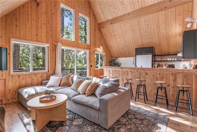 living room featuring beam ceiling, wooden walls, high vaulted ceiling, and light hardwood / wood-style floors