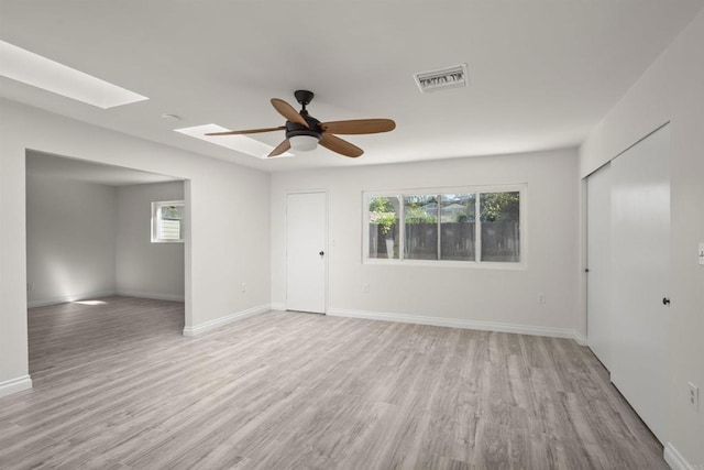 unfurnished room with ceiling fan, a healthy amount of sunlight, light hardwood / wood-style floors, and a skylight