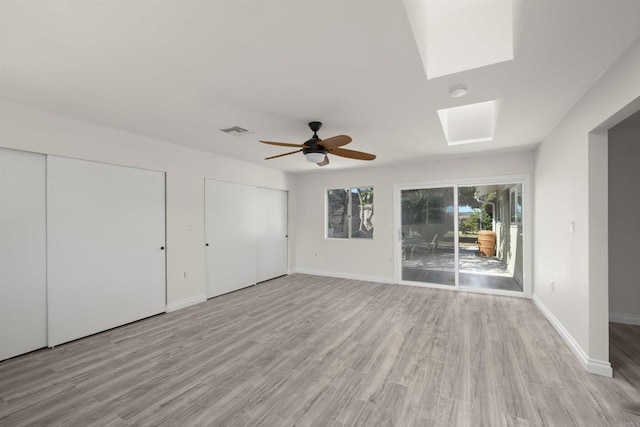 unfurnished bedroom featuring two closets, a skylight, ceiling fan, access to exterior, and light wood-type flooring