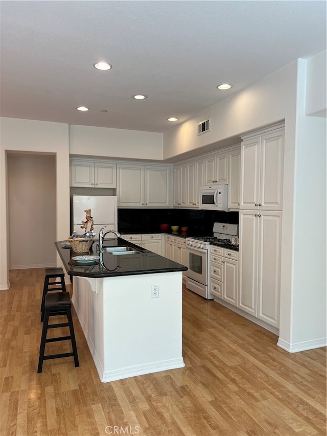 kitchen featuring white appliances, sink, tasteful backsplash, light hardwood / wood-style floors, and a kitchen bar