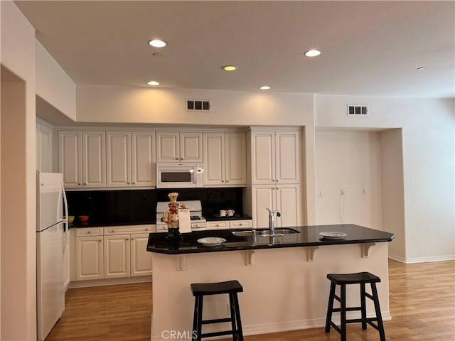 kitchen with white appliances, backsplash, a center island with sink, a kitchen breakfast bar, and sink