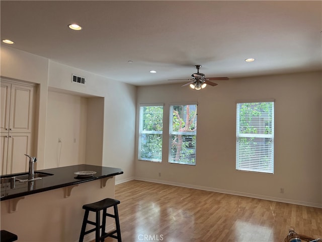 kitchen with a kitchen breakfast bar, ceiling fan, sink, and light hardwood / wood-style flooring