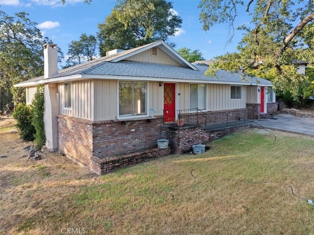 view of front of home featuring a front yard, a chimney, board and batten siding, brick siding, and roof with shingles