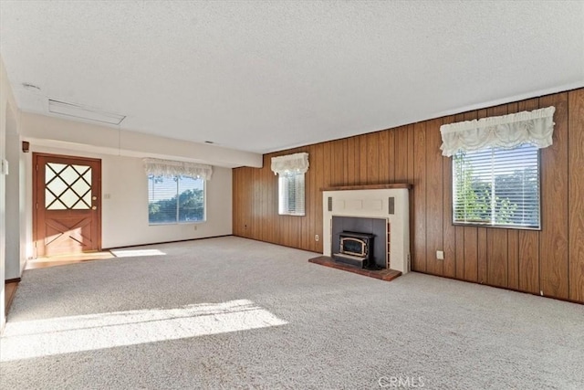 unfurnished living room with a wealth of natural light, a wood stove, a textured ceiling, and carpet floors