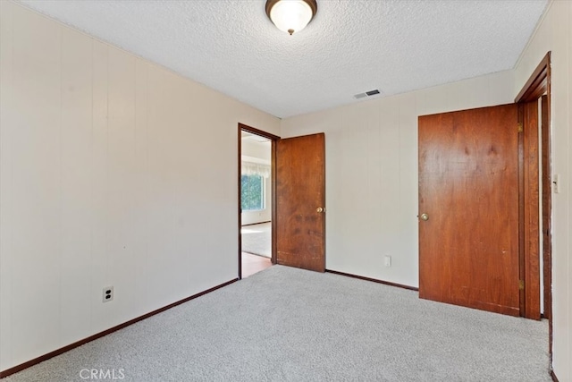 unfurnished bedroom featuring a textured ceiling, light carpet, and a closet