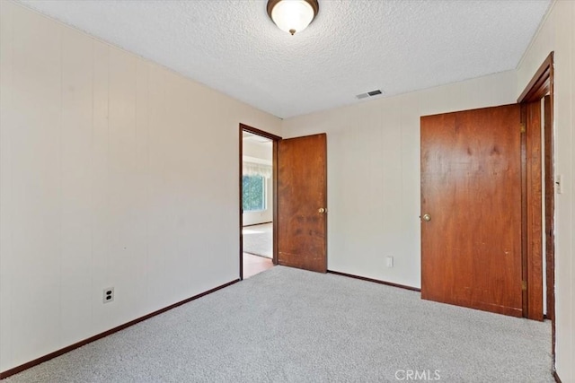 unfurnished bedroom with carpet, visible vents, a textured ceiling, and baseboards