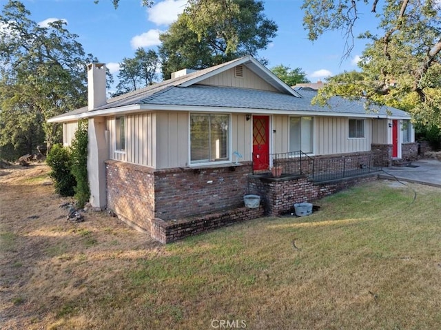 view of front of property featuring board and batten siding, roof with shingles, a front lawn, brick siding, and a chimney