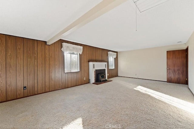 unfurnished living room with a wood stove, carpet floors, attic access, wood walls, and beam ceiling