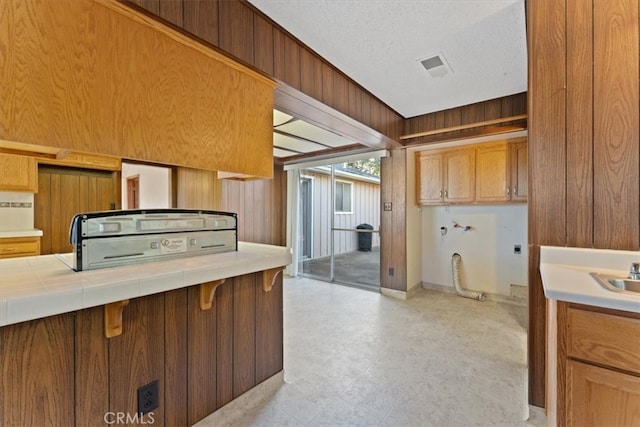 kitchen with a textured ceiling, wooden walls, sink, and tile counters