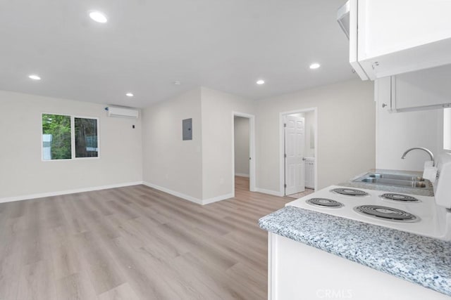 kitchen with electric panel, sink, a wall mounted AC, white cooktop, and light hardwood / wood-style floors