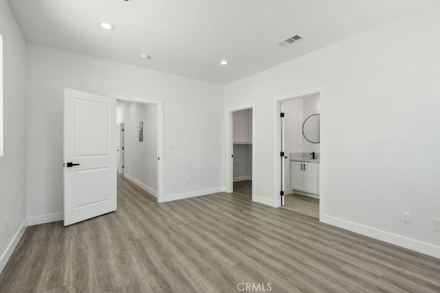 unfurnished bedroom featuring a walk in closet, ensuite bathroom, a closet, and light wood-type flooring