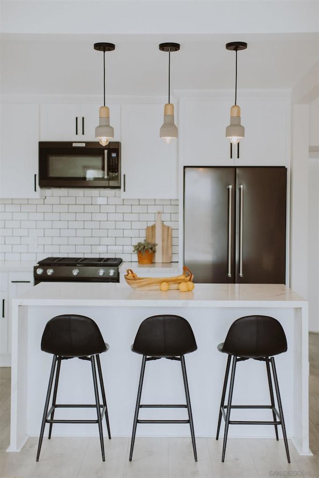 kitchen with a breakfast bar area, decorative light fixtures, backsplash, white cabinets, and black appliances