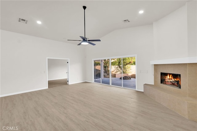 unfurnished living room with ceiling fan, light wood-type flooring, a tile fireplace, and vaulted ceiling