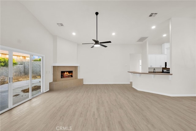 unfurnished living room featuring ceiling fan, a tiled fireplace, a towering ceiling, and light hardwood / wood-style flooring