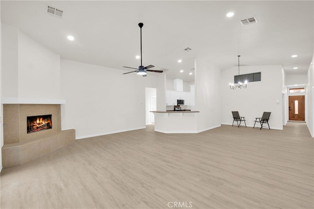 unfurnished living room with ceiling fan with notable chandelier, light wood-type flooring, a fireplace, and vaulted ceiling