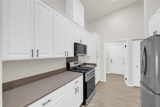 kitchen with white cabinetry, stainless steel appliances, a high ceiling, and light hardwood / wood-style floors