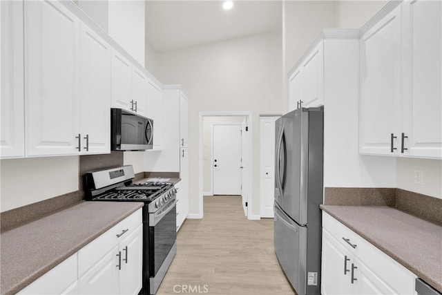 kitchen with appliances with stainless steel finishes, a towering ceiling, light hardwood / wood-style flooring, and white cabinetry