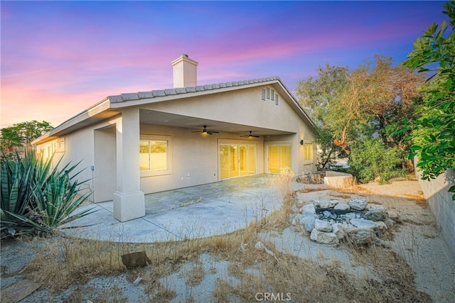 back house at dusk with ceiling fan and a patio area