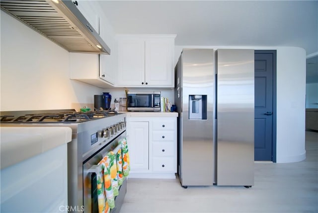 kitchen featuring white cabinets, stainless steel appliances, wall chimney range hood, and light wood-type flooring