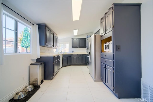 kitchen featuring stainless steel fridge, white microwave, a wealth of natural light, and lofted ceiling