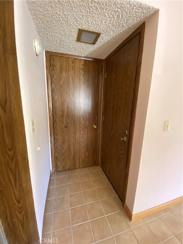 hall featuring a textured ceiling and light tile patterned floors