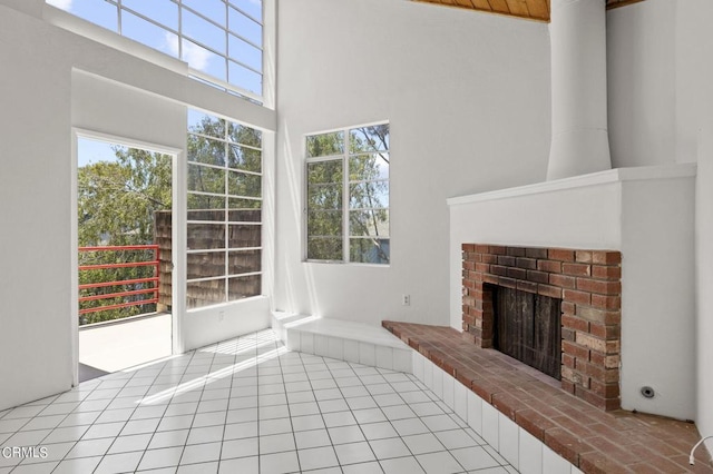 unfurnished living room with light tile patterned floors, a high ceiling, and a brick fireplace