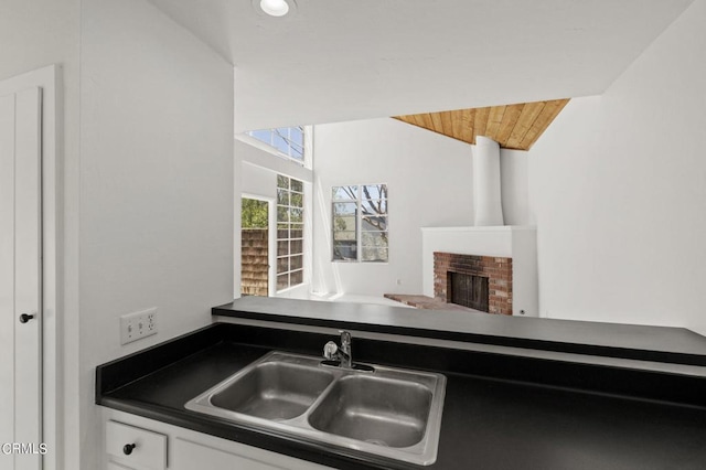 kitchen featuring a fireplace, white cabinetry, wooden ceiling, and sink