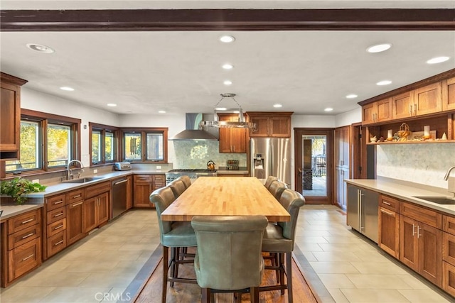 kitchen with a breakfast bar, a center island, wall chimney range hood, sink, and appliances with stainless steel finishes