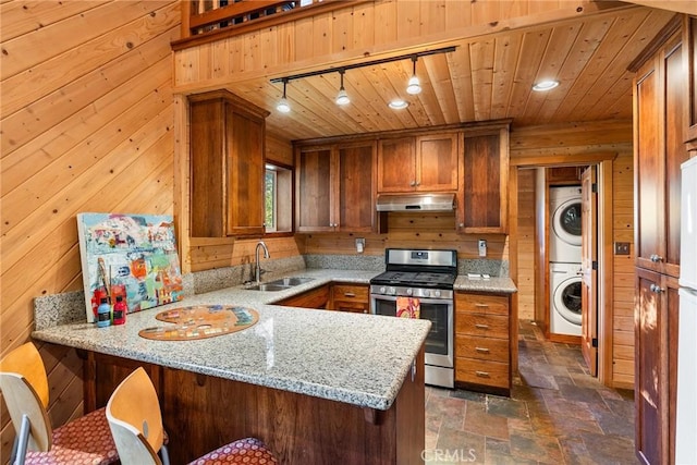 kitchen with kitchen peninsula, rail lighting, stainless steel gas range, sink, and stacked washer / drying machine