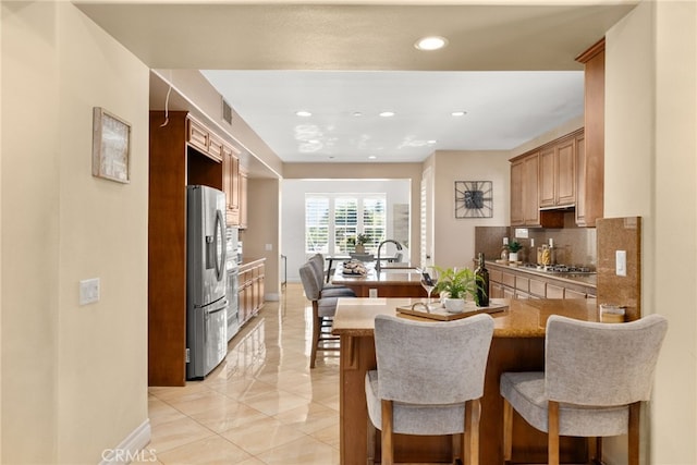 kitchen featuring kitchen peninsula, tasteful backsplash, appliances with stainless steel finishes, a kitchen bar, and sink