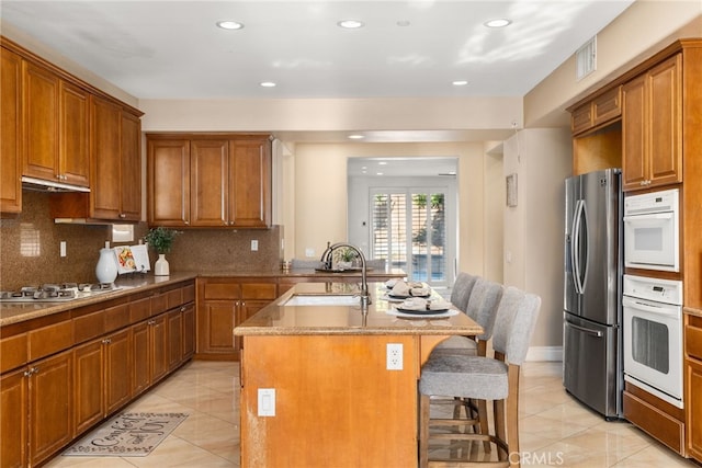 kitchen with backsplash, a breakfast bar, a kitchen island with sink, sink, and white appliances