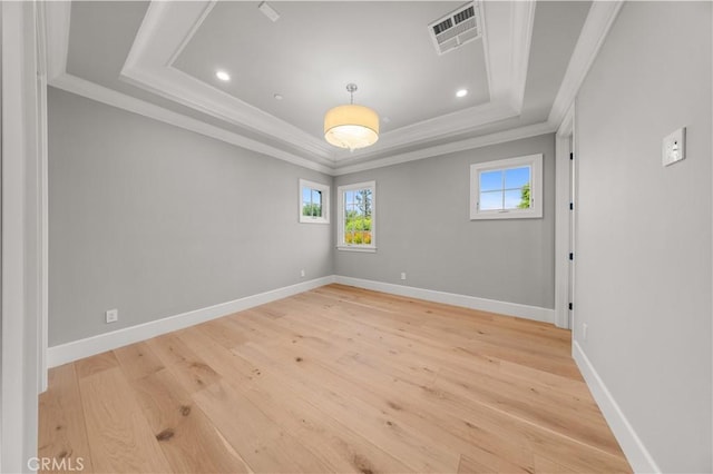 empty room featuring a tray ceiling, ornamental molding, and light wood-type flooring