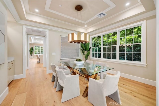 dining room featuring a raised ceiling, crown molding, and light hardwood / wood-style flooring